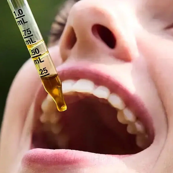 Close-up of a mouth with a dropper filled with liquid held above it.