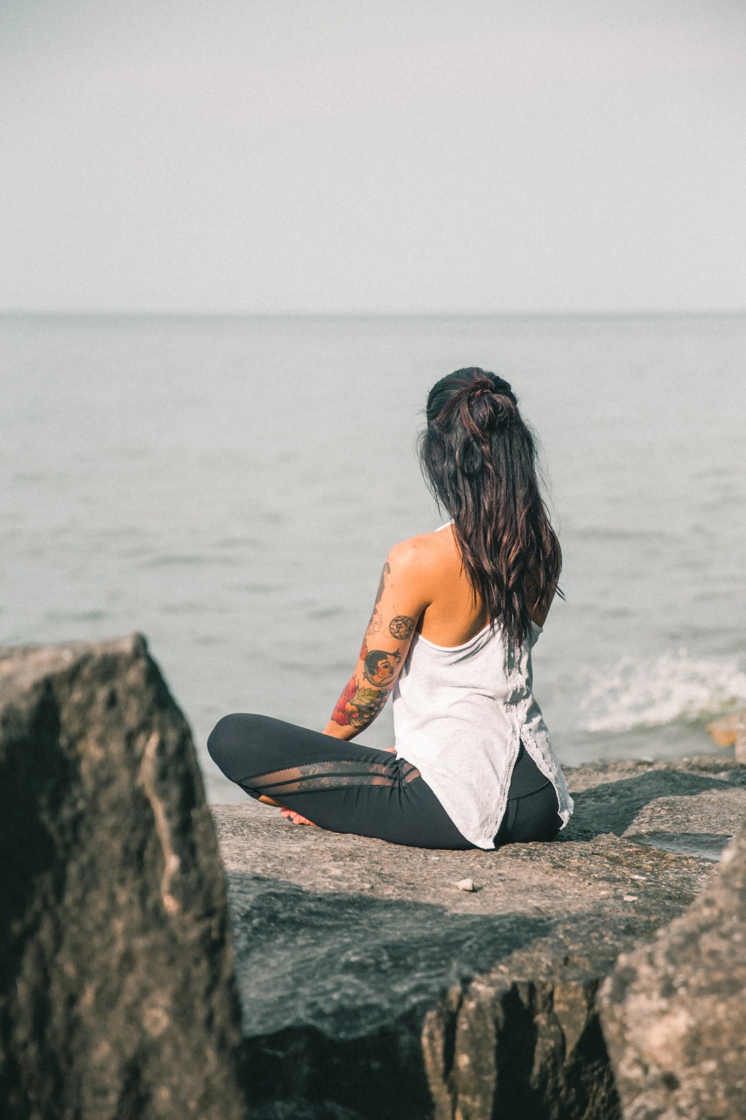 beautiful tattooed yoga woman meditating by ocean 